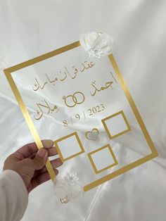 a person holding up a wedding card in front of a white sheet with gold foil