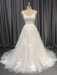 a white wedding dress on display in front of grey curtained backdrop with curtains behind it