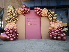 a large arch made out of balloons on the side of a building with a pink door