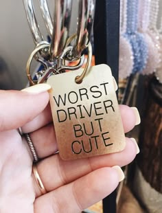 a person holding a keychain that says worst driver but cute