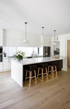 a large kitchen with white cabinets and wooden flooring, along with bar stools