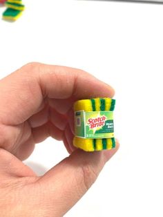 a hand holding a small yellow and green eraser on top of a white surface