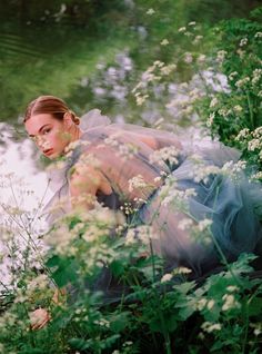 a woman laying on the ground in front of flowers and water with her head down