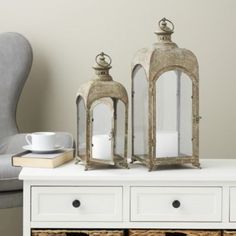 two lanterns sitting on top of a white table next to a chair and coffee cup