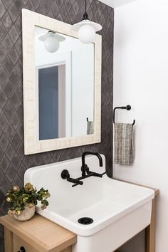 a white sink sitting under a bathroom mirror next to a wooden table with a potted plant on it