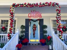 christmas decorations on the front porch of a white house with red and gold ornaments hanging from it