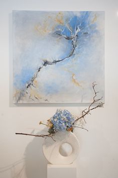 a painting on the wall above a vase with blue flowers in it and a white sculpture