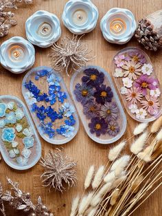 several trays filled with flowers and candles on top of a wooden table next to dry grass