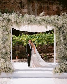 a bride and groom standing in front of an archway with greenery on the sides