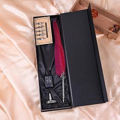 an open box with a red feather, pen and bottle opener in it on a bed