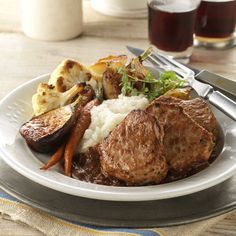 a white plate topped with meat, potatoes and carrots next to a glass of wine