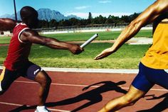 two men are running on a track with one holding a baton and the other reaching out