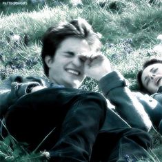 two people laying in the grass with one holding his hand up to his ear and smiling