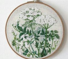 a white flower embroidery is hanging on a wooden hoop, with green and white flowers in the center