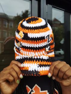 a person wearing an orange and black striped knitted hat holding up their face to the camera