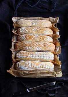 four loaves of bread sitting in a brown paper bag on top of a black cloth