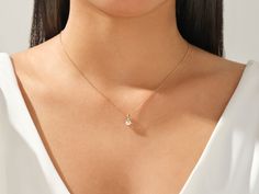 a woman wearing a gold necklace with a small white diamond on the end of it