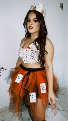 a woman wearing a red tutu with cards on her skirt and tiara, standing in front of a white wall