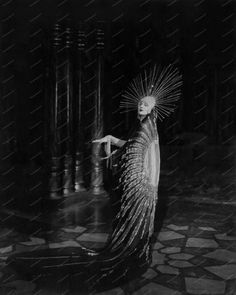 an old fashion photo of a woman with feathers on her head and arms, standing in front of columns