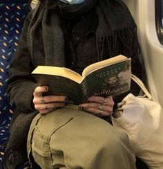 a woman reading a book while sitting on a subway train with her face covered by a mask