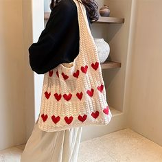 a woman carrying a knitted bag with red hearts on the front and bottom, in white