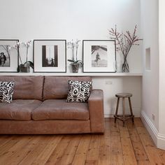 a brown leather couch sitting in a living room next to a white wall with pictures on it