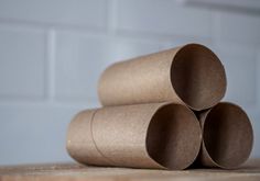 three rolled up brown paper tubes sitting on top of a wooden table next to a white brick wall