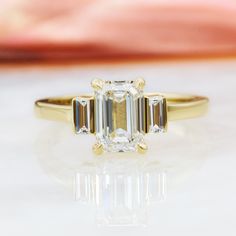 Reverie– an Art Deco-inspired engagement ring of timeless elegance. Crafted in yellow gold, this stunning piece features a 1.25-carat emerald-cut natural diamond, ethically sourced and earth-mined. Adorned with 0.25 carats of baguette-shaped accent diamonds, the Reverie radiates vintage charm and modern sophistication. With a total carat weight of 1.5, this ring is a testament to enduring love and ethical luxury, perfect for those who appreciate classic beauty and refined design. Diana Rafael di Black Diamond Necklace, Black Diamond Studs, Emerald Cut Diamond Engagement Ring, White Diamond Earrings, Emerald Cut Diamond Engagement, Black Diamond Earrings, Halo Necklace, Black Diamond Ring Engagement, Golden Ring