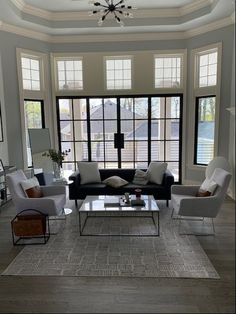 a living room with couches, chairs and a coffee table in front of large windows