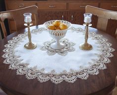 a table topped with a bowl of oranges on top of a white doily