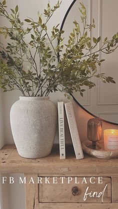 a white vase sitting on top of a wooden table next to a book and candle