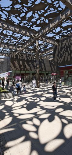 people are walking around in an open area with shadows on the floor and ceiling above them