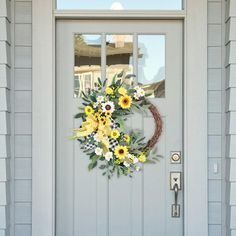 a wreath with yellow and white flowers is hanging on the front door of a house