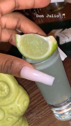 a person holding a lime in their hand next to a glass filled with water and liquid