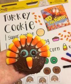 a hand holding a chocolate turkey cookie in front of a thanksgiving themed activity board with crayons