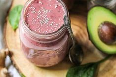 two jars filled with smoothie sitting on top of a cutting board next to an avocado