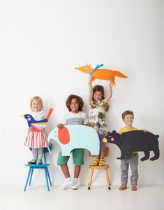 three children standing in front of a white wall holding up paper cutouts with animals on them