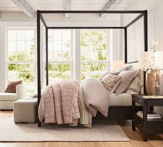 a bedroom with a four poster bed and white walls, hardwood flooring and windows