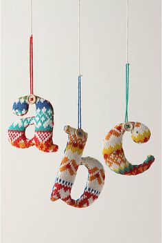 three knitted ornaments hanging from strings in the shape of numbers