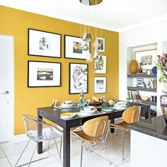 a dining room with yellow walls and pictures hanging on the wall above the dinning table