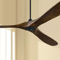 a wooden ceiling fan hanging from the ceiling in a room with white walls and windows