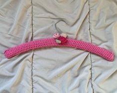 a pink crocheted hanger with flowers on it sitting on a white sheet