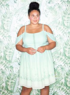 a woman standing in front of a wall with leaves on it and wearing a green dress