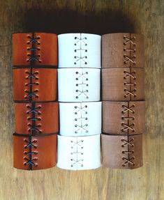 four different types of leather bracelets are lined up on a wooden surface, one is brown and the other is white