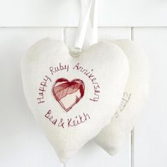 two white heart shaped cushions hanging from hooks on a wall with the words happy ruby anns and beth written on them