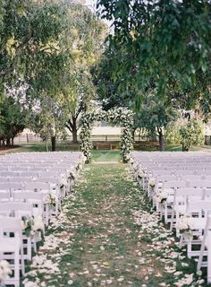 an outdoor wedding ceremony with white chairs and flowers on the aisle, surrounded by trees