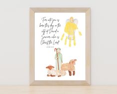 a framed print with an angel and sheep on it, in front of a white wall