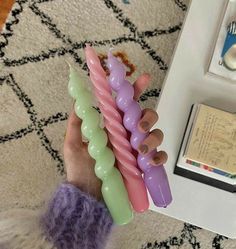 a person holding three different colored candles in their hands on a rug next to a table