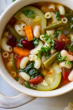 a white bowl filled with pasta and veggies soup on top of a table