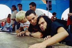 three men leaning on a table in front of a group of people